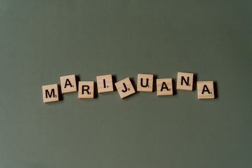 Free Scrabble tiles arranged to spell 'Marijuana' against a green backdrop in a minimalist style. Stock Photo