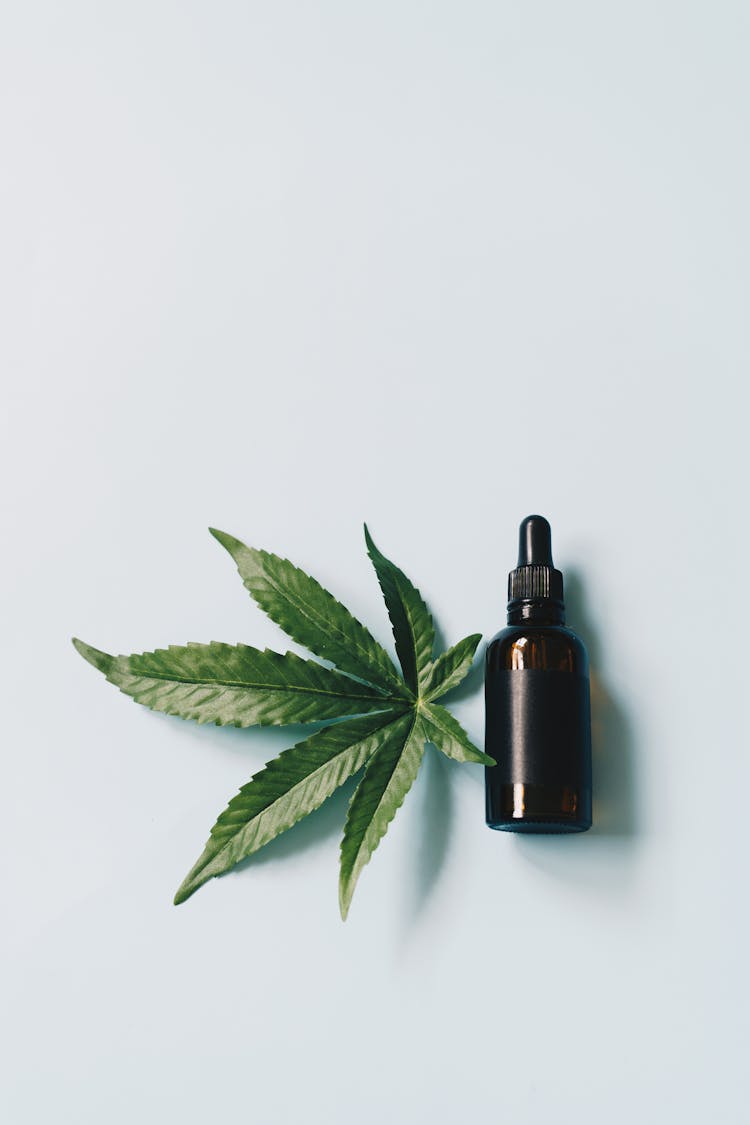 Serum Bottle And A Leaf Of Marijuana On A White Surface