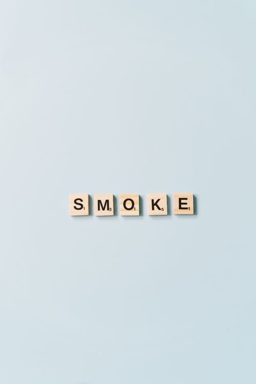 Free Scrabble tiles arranged to spell 'Smoke' on a light blue background, minimalist design. Stock Photo