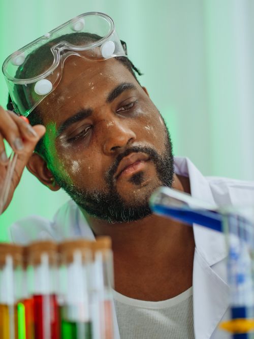 Free A focused scientist with protective goggles analyzes colorful test tubes in a lab. Stock Photo