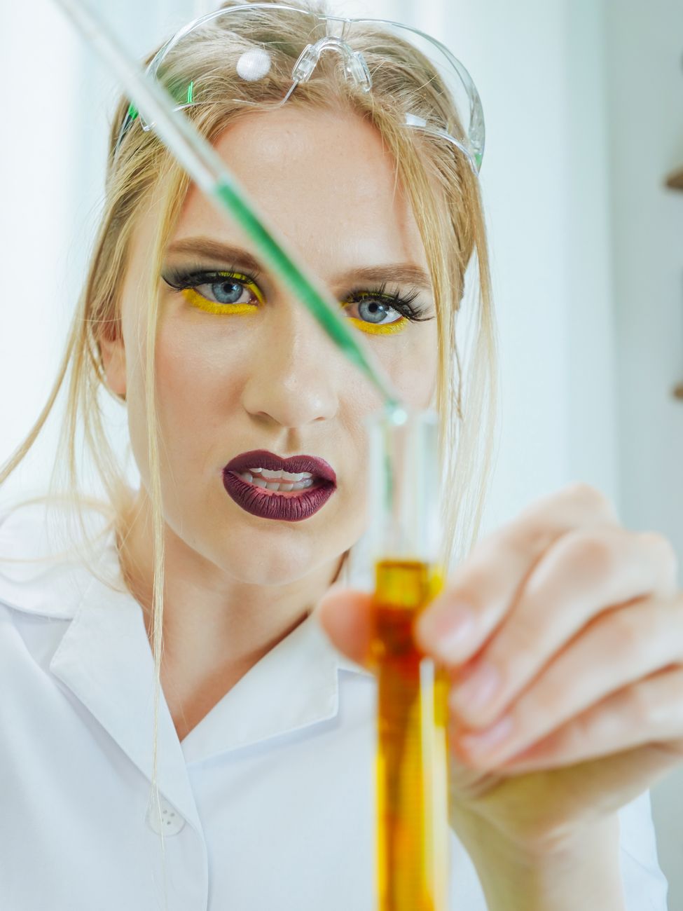 Woman in lab coat using pipette with colorful makeup showcasing focus and concentration in laboratory.
