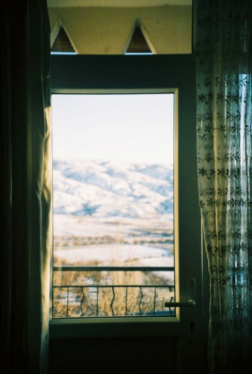 Free A tranquil view of a snowy mountain range seen through a window with curtains, evoking peace. Stock Photo