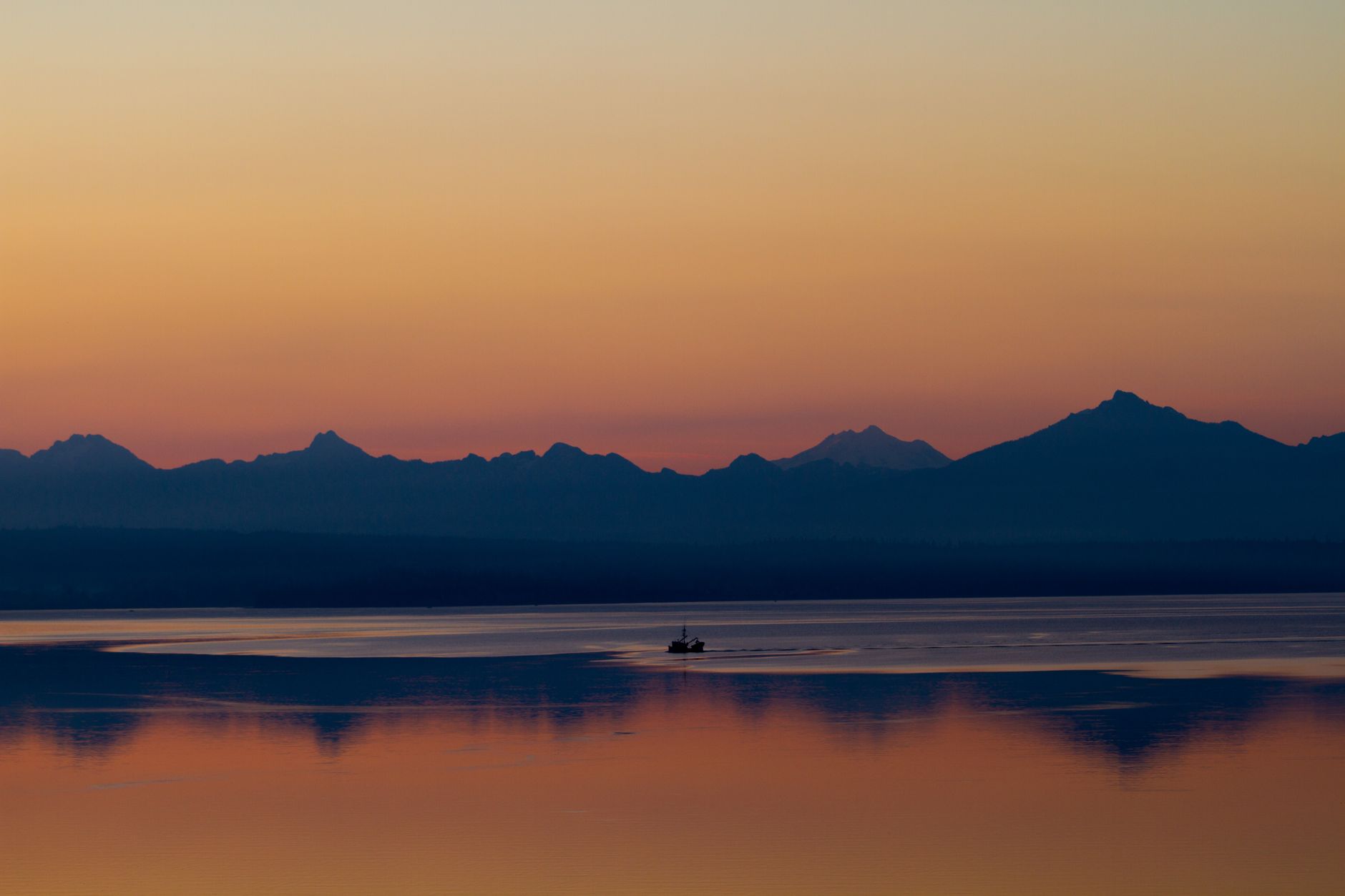 Serene sunrise over the mountains reflecting on Puget Sound with a lonely boat silhouetted against a vibrant sky.