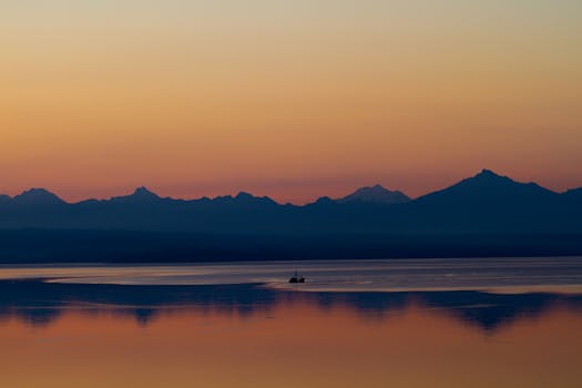Serene sunrise over the mountains reflecting on Puget Sound with a lonely boat silhouetted against a vibrant sky.