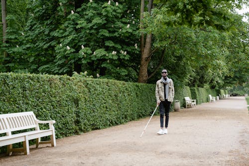 Man Holding a White Cane While Walking at the Park