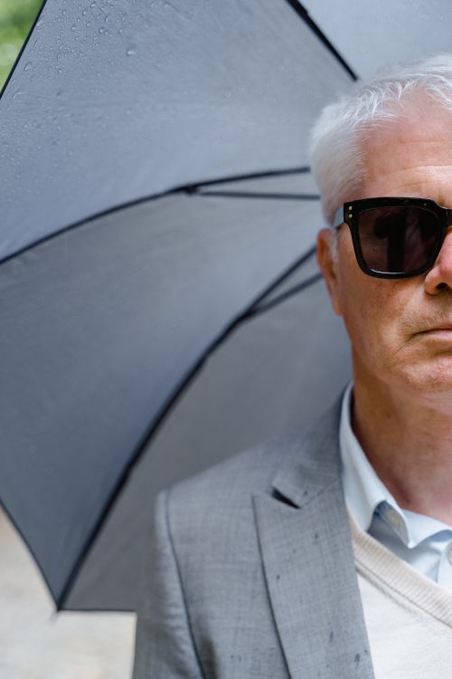 Free Senior man in gray suit and sunglasses holding an umbrella outdoors. Stock Photo