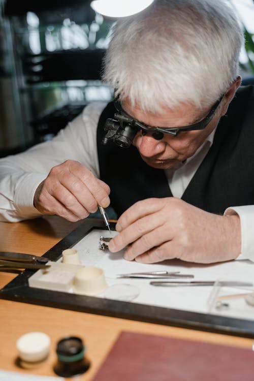 A Man with White Hair Fixing a Watch while Wearing Magnifying Loupe Glass