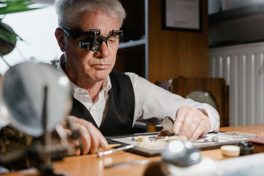 Elderly watchmaker using magnifying glasses to repair a precision timepiece in his workshop.