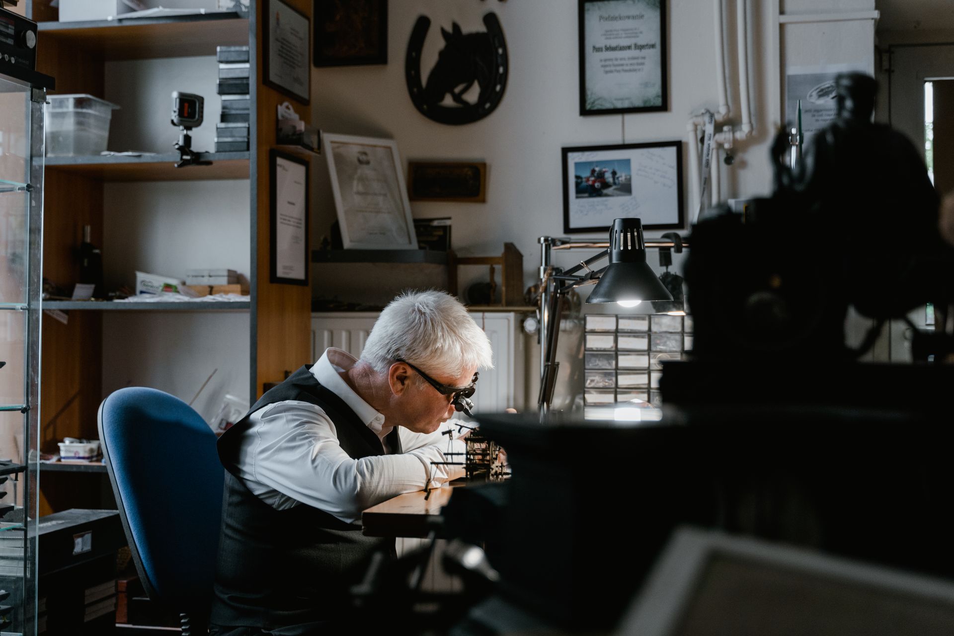Elderly man concentrating on work at a cluttered desk in a cozy office setting.