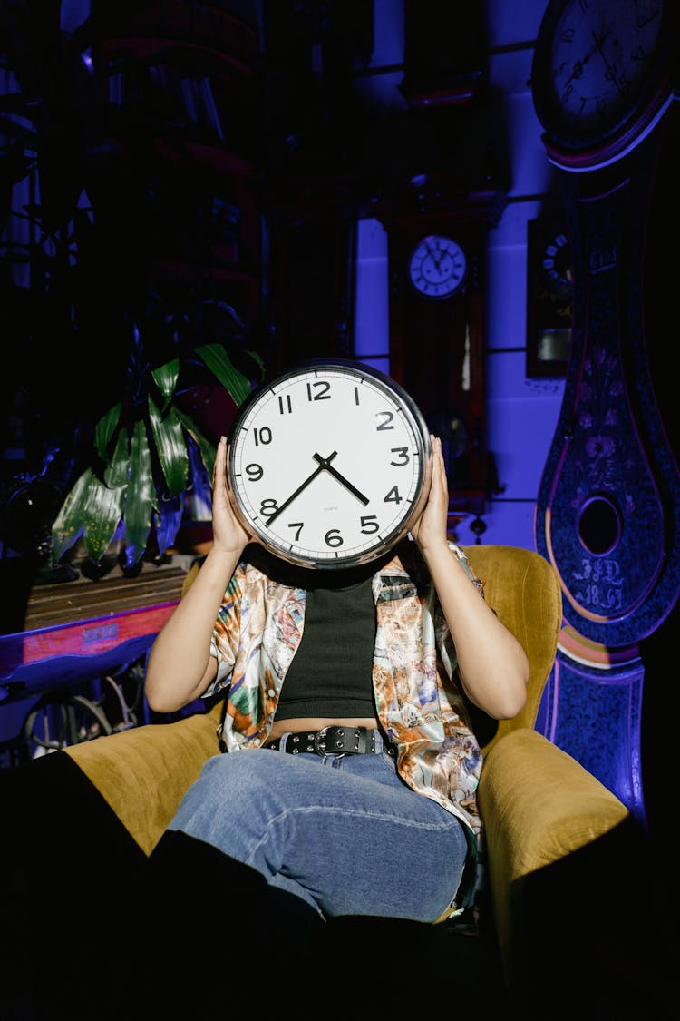 A Person Holding A Wall Clock Near Her Face 