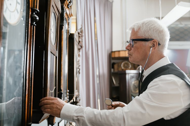 An Elderly Man Wearing Stethoscope Standing While Looking At The Vintage Clock On The Wall