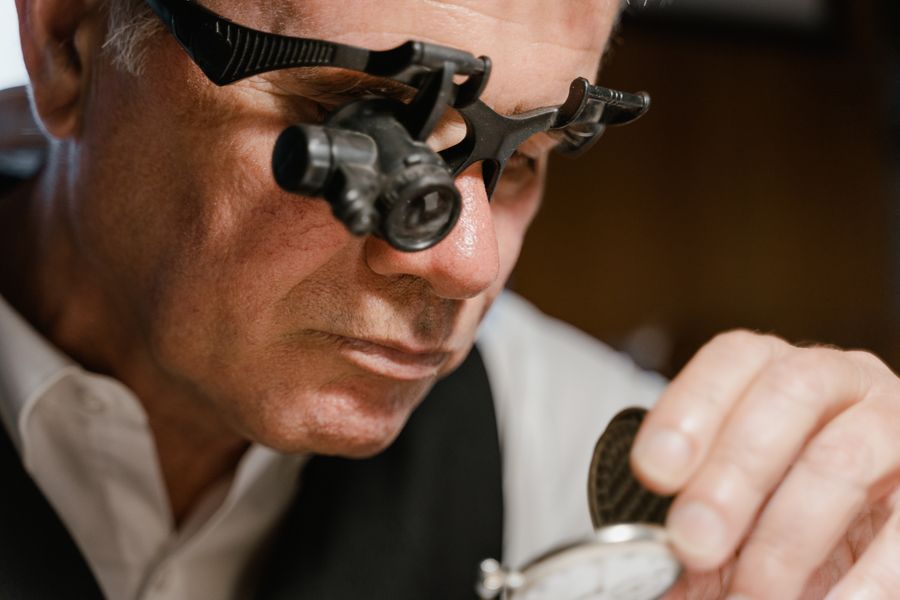 Laikrodininkas su lupos akiniais tikrina laikrodžio mechanizmą — laikrodžių remontas Alytuje