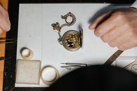 A detailed view of a vintage pocket watch being repaired on a workbench by a craftsman.