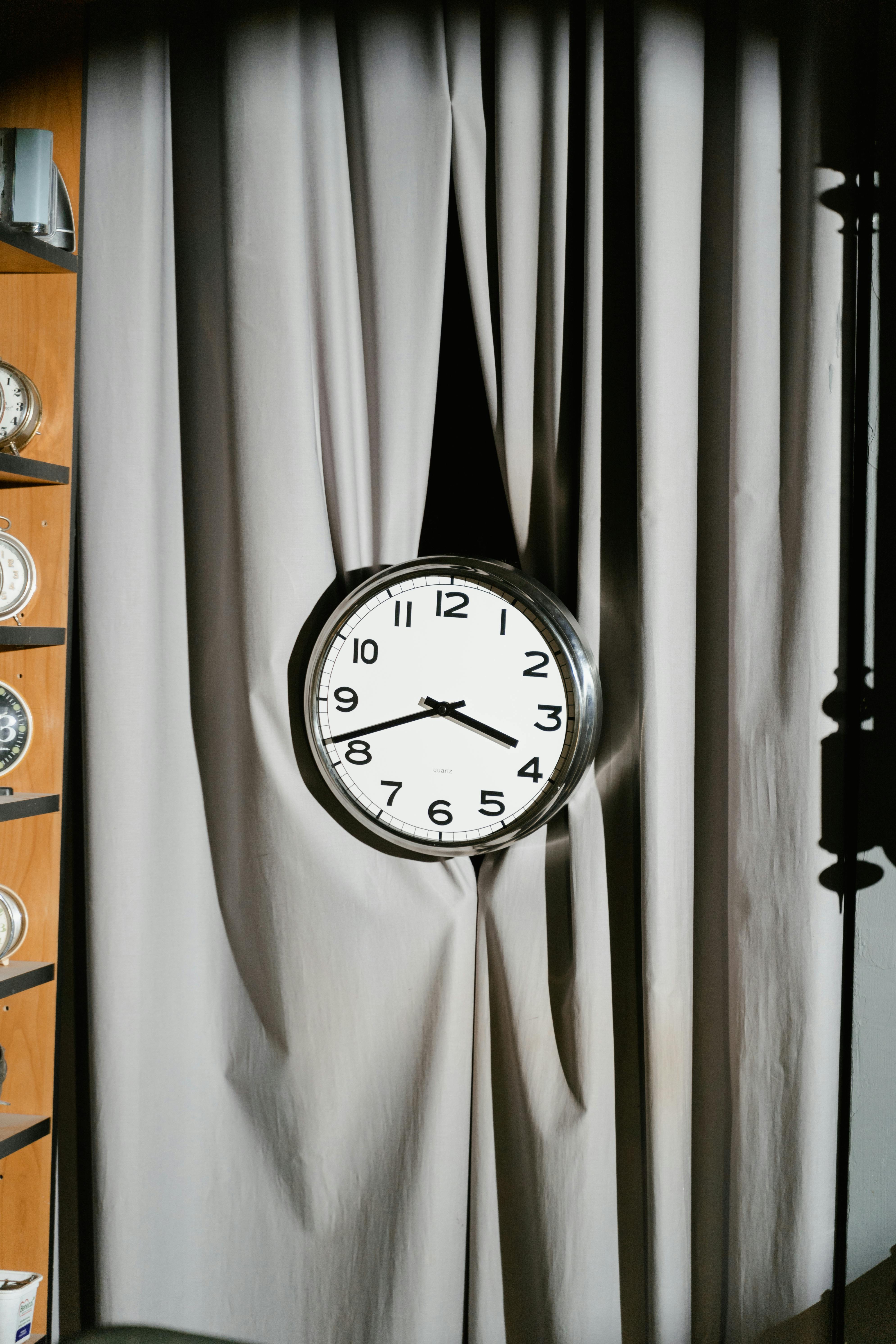 A classic wall clock hanging on a grey curtain, casting a shadow.