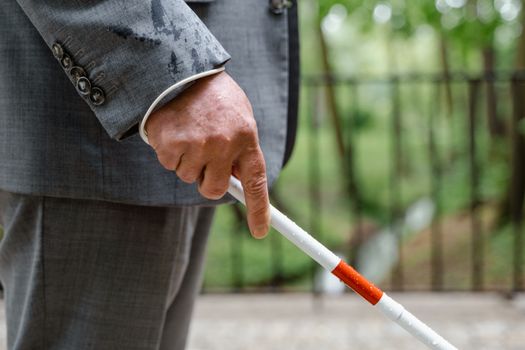 A close-up of a man's hand holding a white cane, symbolizing visual impairment.