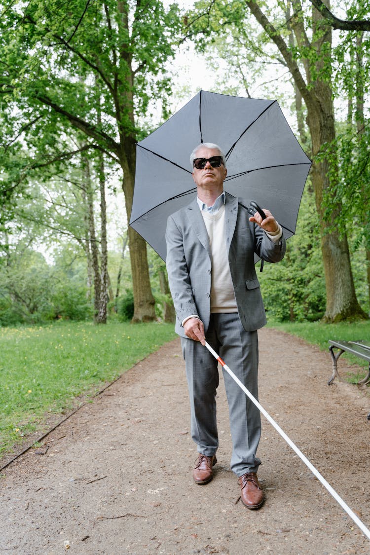 An Elderly Man Holding An Umbrella While Using A Walking Stick