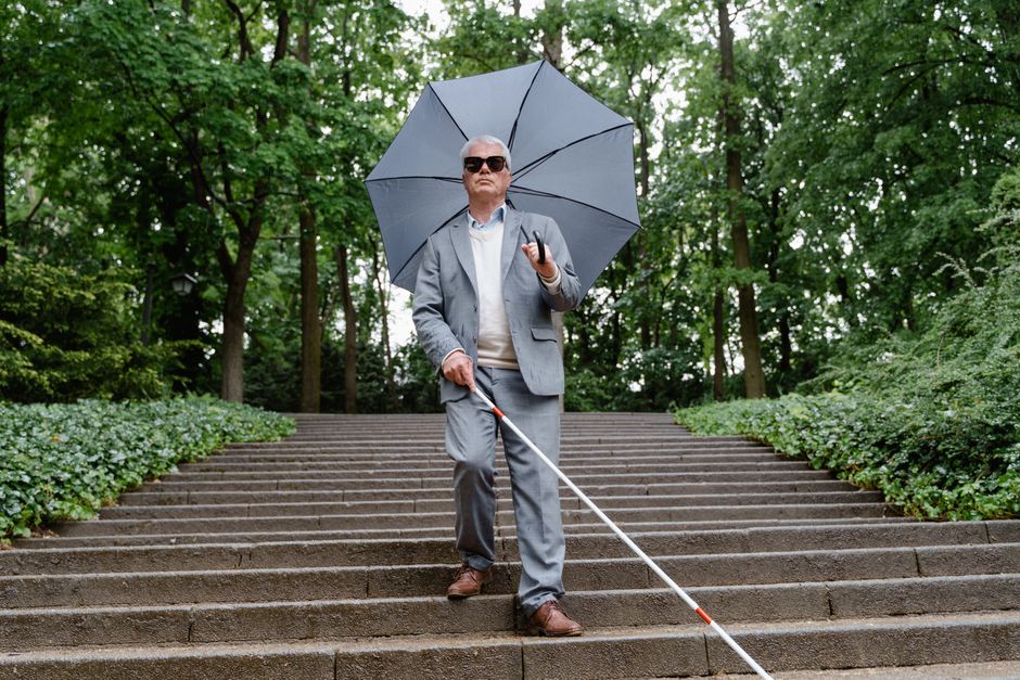 Mature man with visual impairment walking down outdoor stairs using cane.