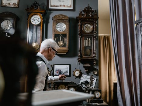 Watchmaker in vintage repair shop surrounded by antique wall clocks and intricate timepieces.