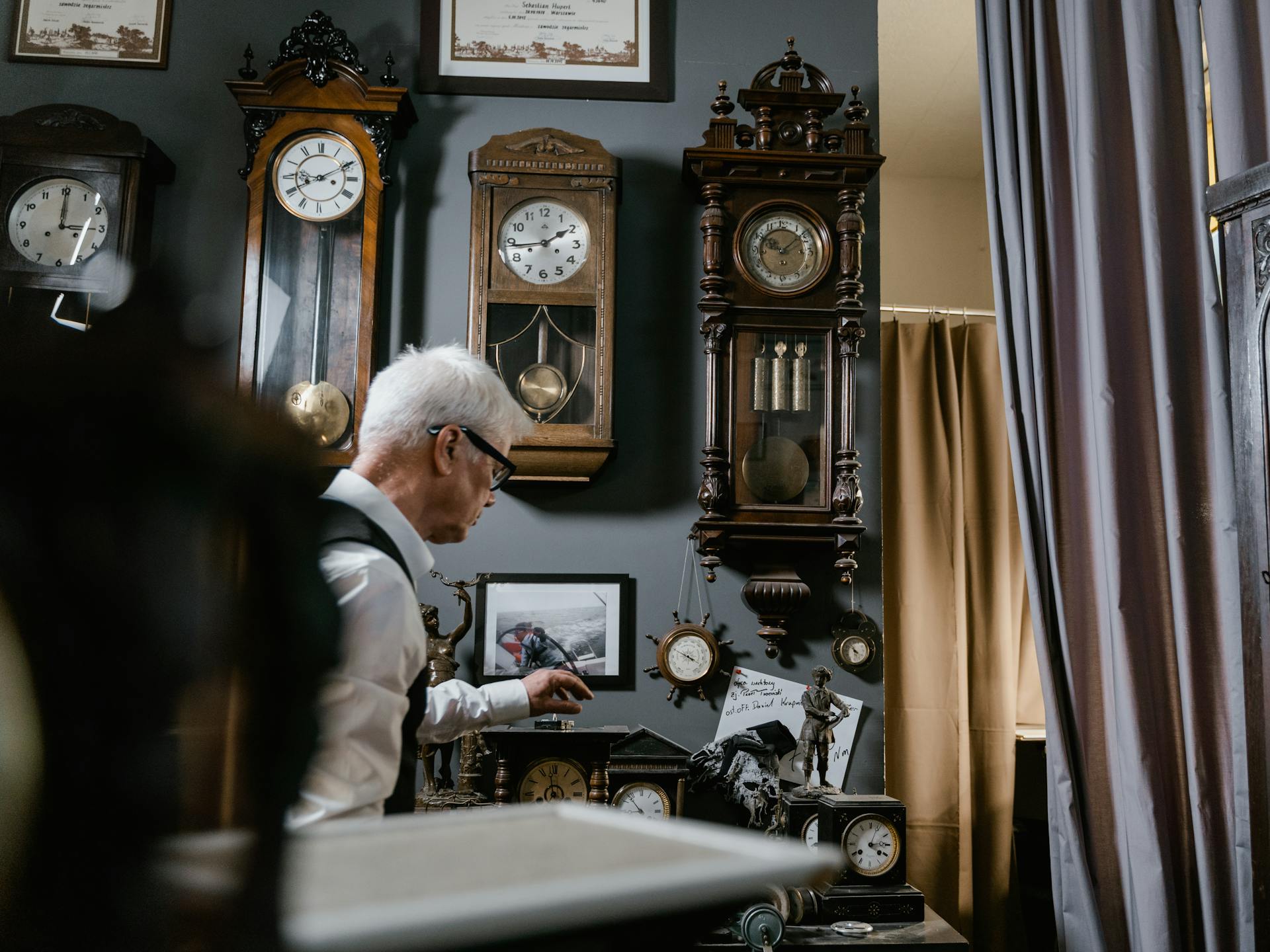 Watchmaker in vintage repair shop surrounded by antique wall clocks and intricate timepieces.