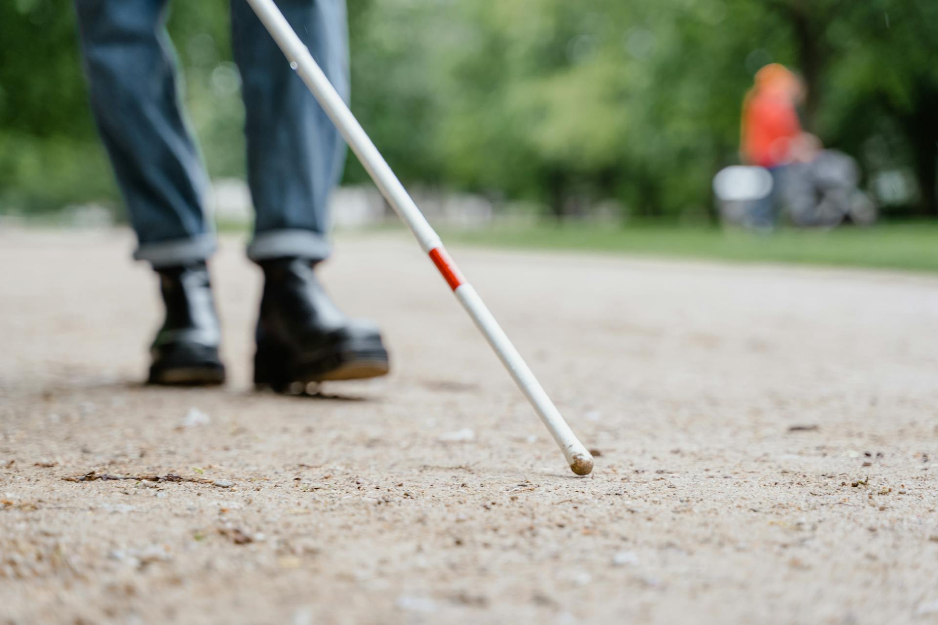 Close-up of a walking stick used by a visually impaired person in a park, symbolizing independence and mobility.