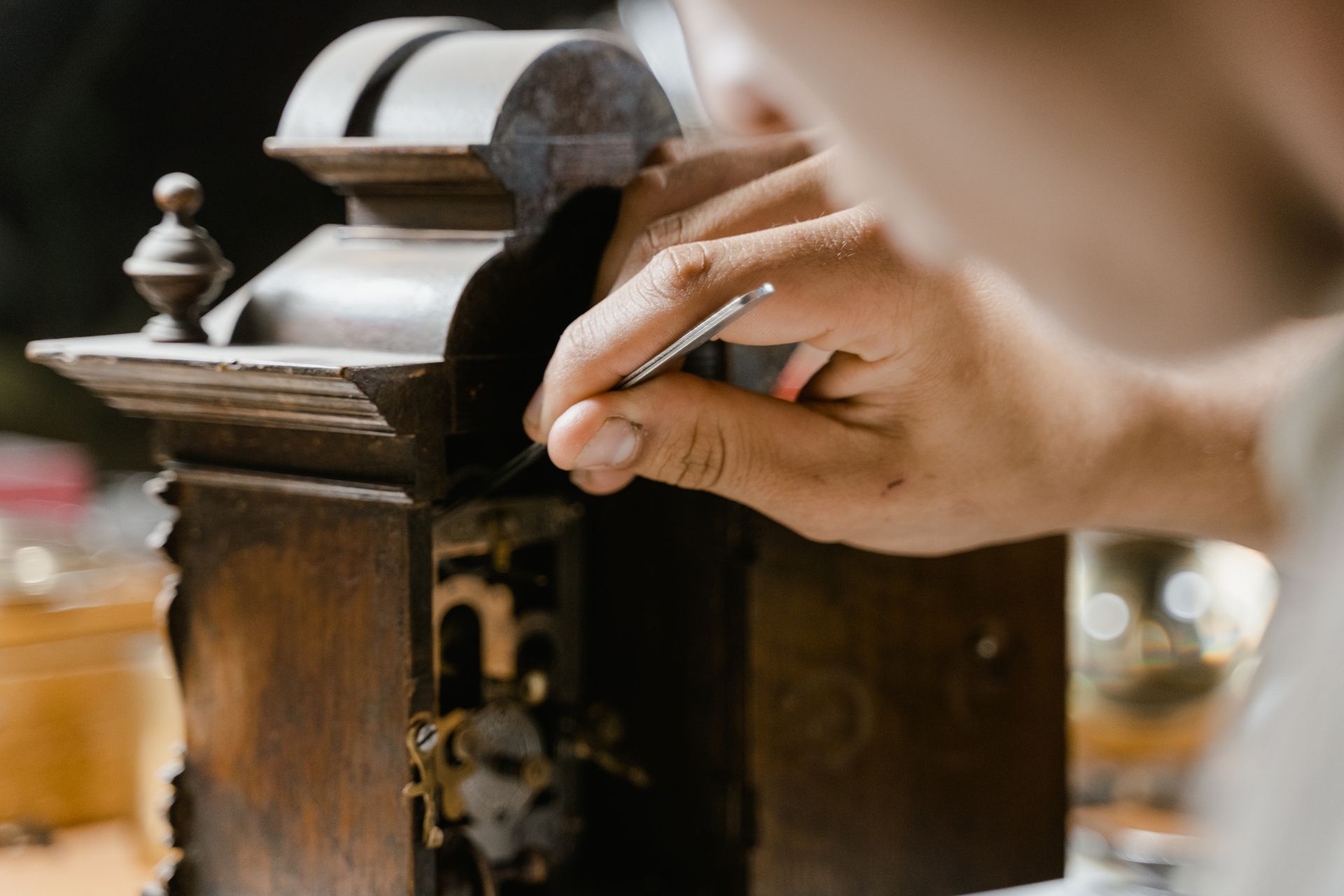 Close-up of hands skillfully restoring an antique wooden clock, highlighting craftsmanship.