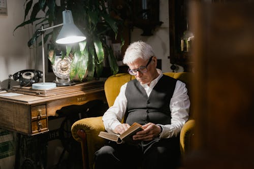 Elderly Man in Eyeglasses Sitting on Armchair while Holding a Book