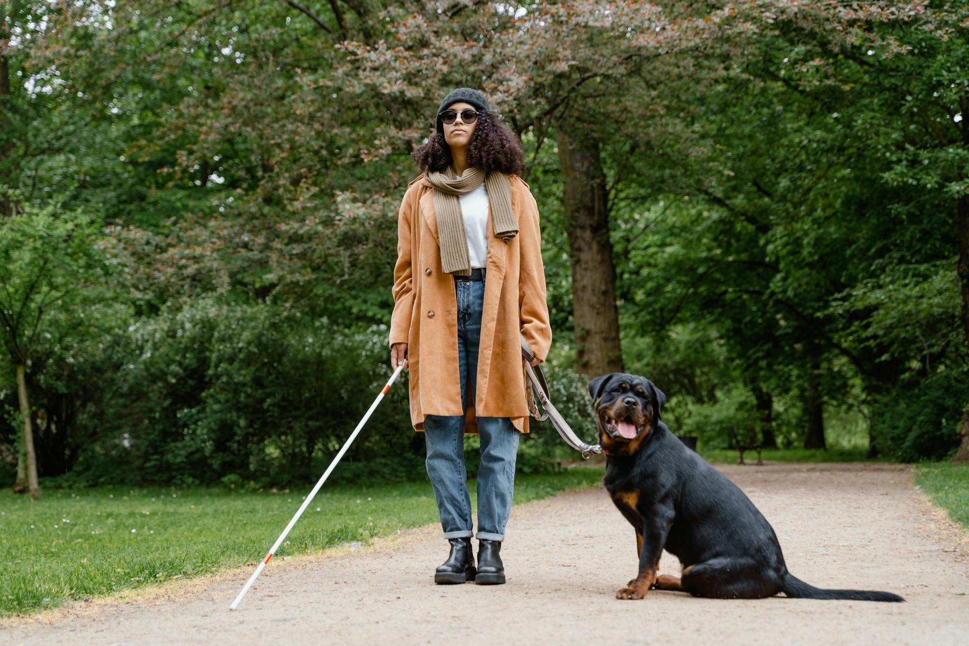 Kvinna i brun kappa och blå jeans står bredvid en ledarhund