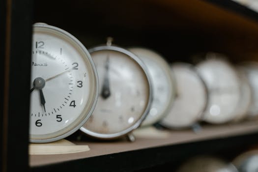A collection of vintage analog alarm clocks displayed on a wooden shelf with blurred background.