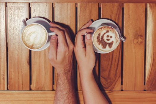Two adults holding cups of coffee with intricate latte art on a wooden table.