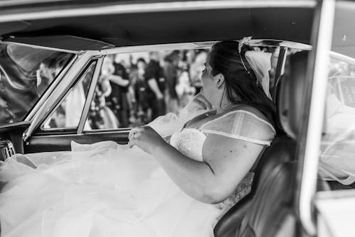 Grayscale Photo of Woman in Wedding Dress Sitting in a Car
