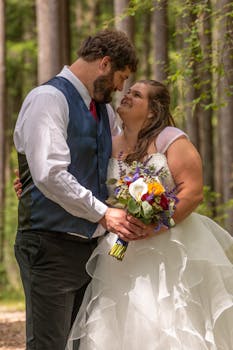A joyful bride and groom embrace amidst lush forest greenery, capturing a tender wedding moment.
