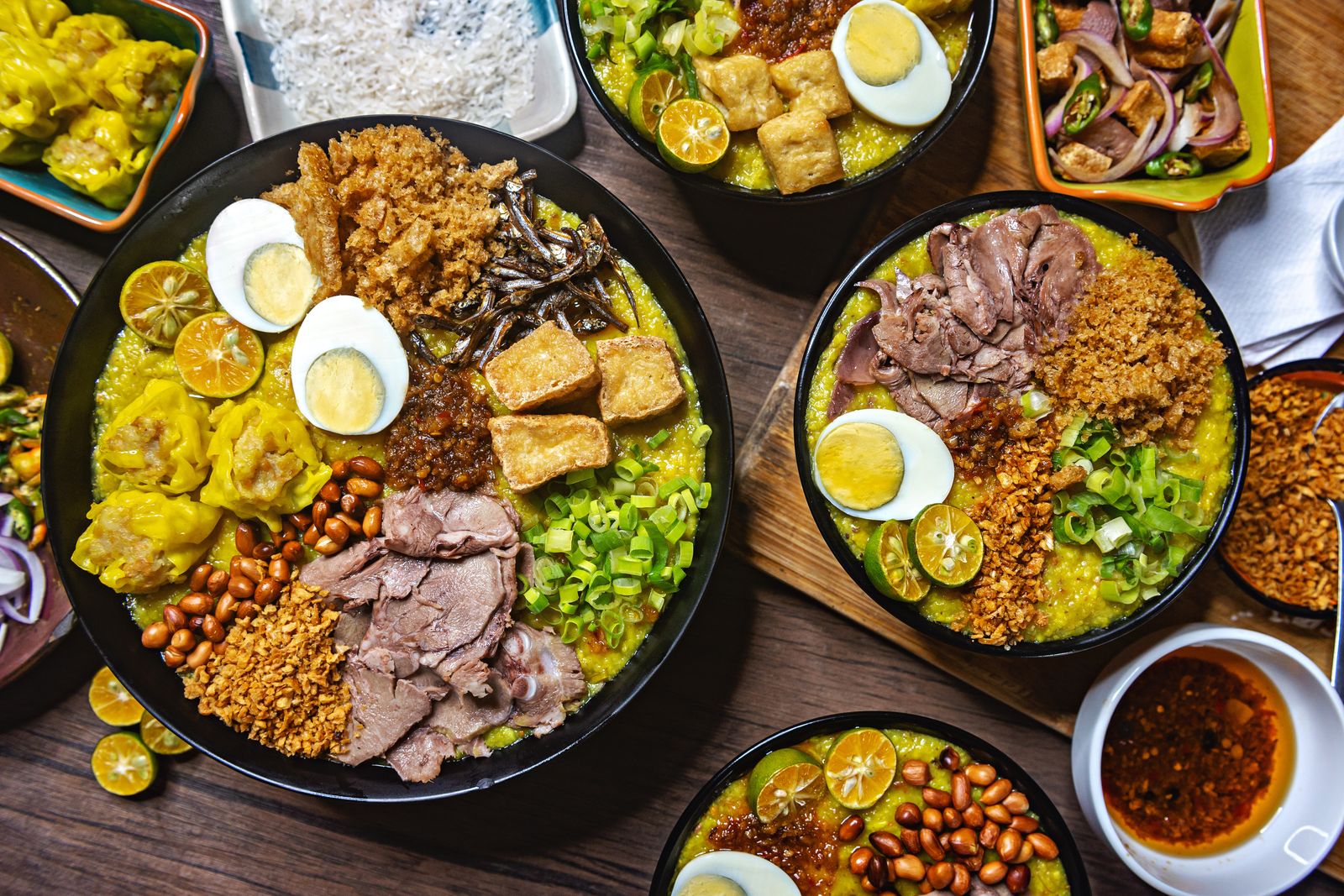 Colorful bowls of Filipino Arroz Caldo with various delicious toppings on a wooden table.