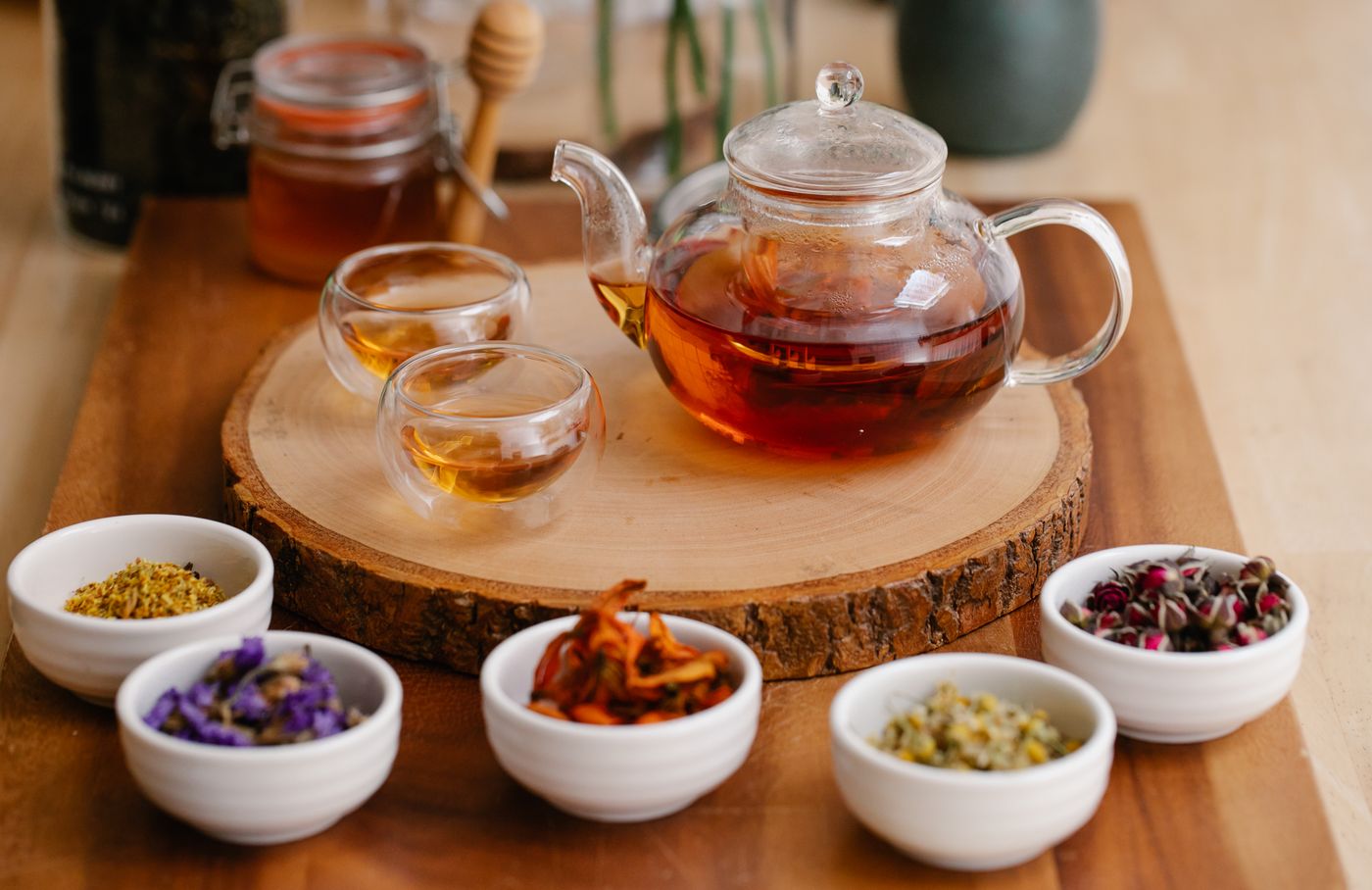 A glass teapot and cups of herbal infusion with fresh herbs on a wooden tray