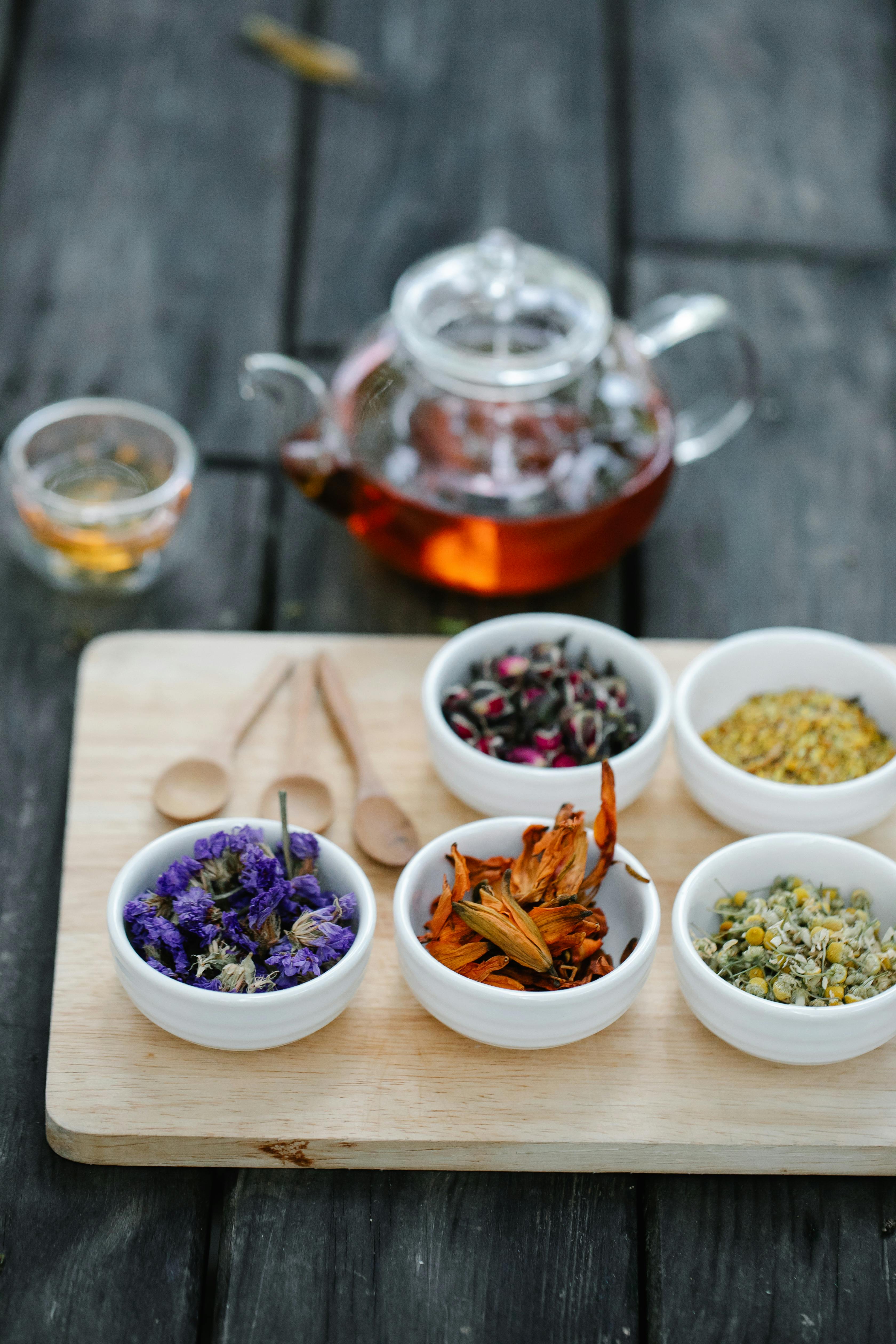 multicoloured herbs in ceramic bowls and tea brewing in a pot