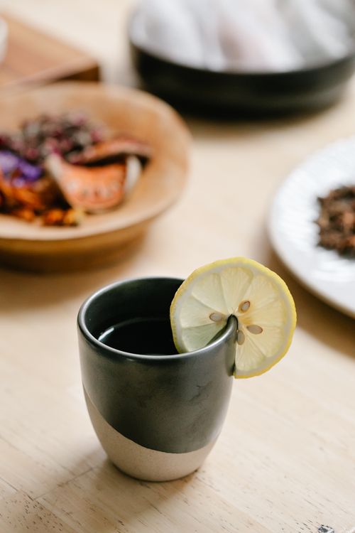 Free A warm cup of tea with a lemon slice, surrounded by bowls of dried herbs for a calming experience. Stock Photo