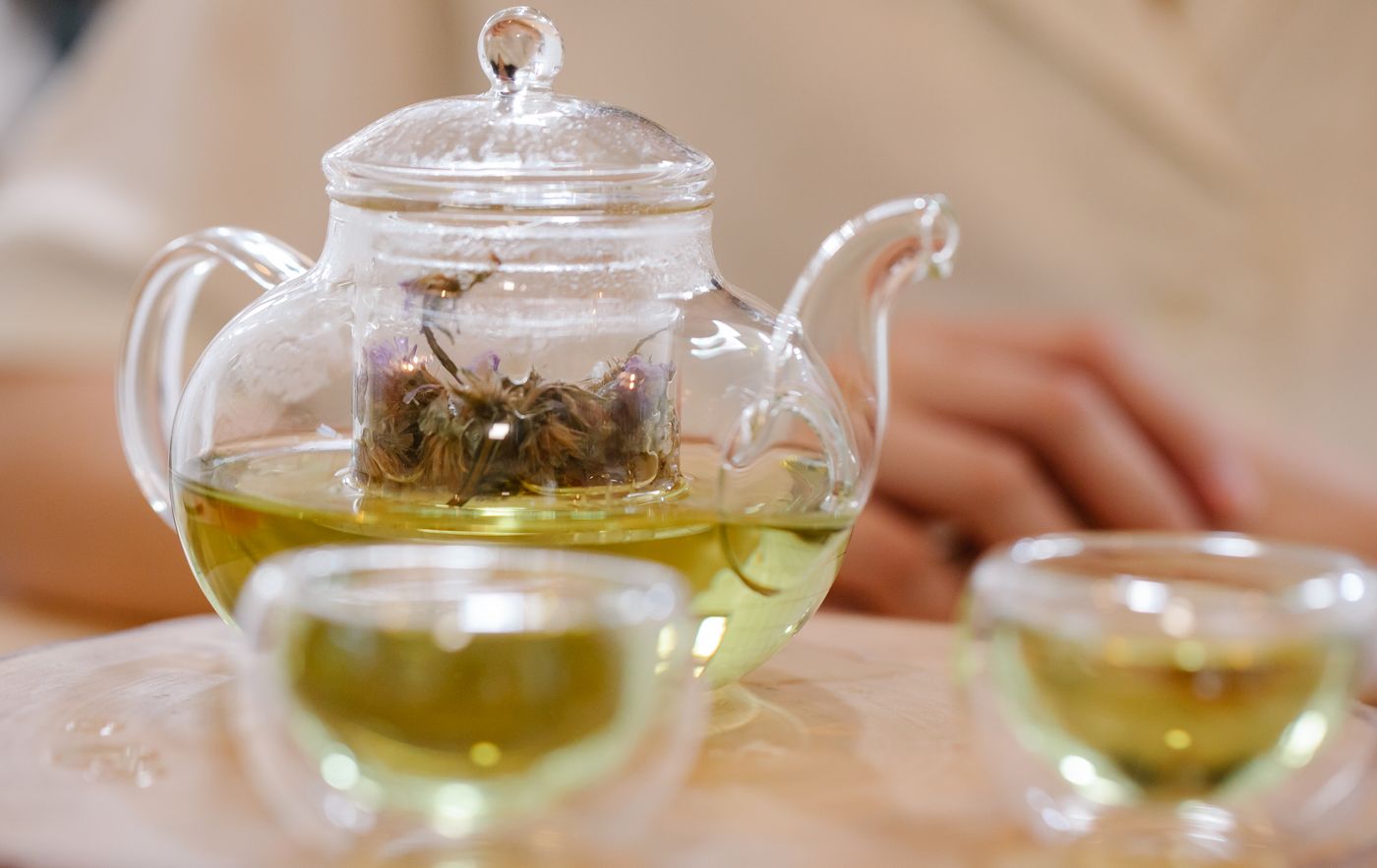 Glass teapot and cups of brewed green tea, showing tea to water ratio scaled up to a pot