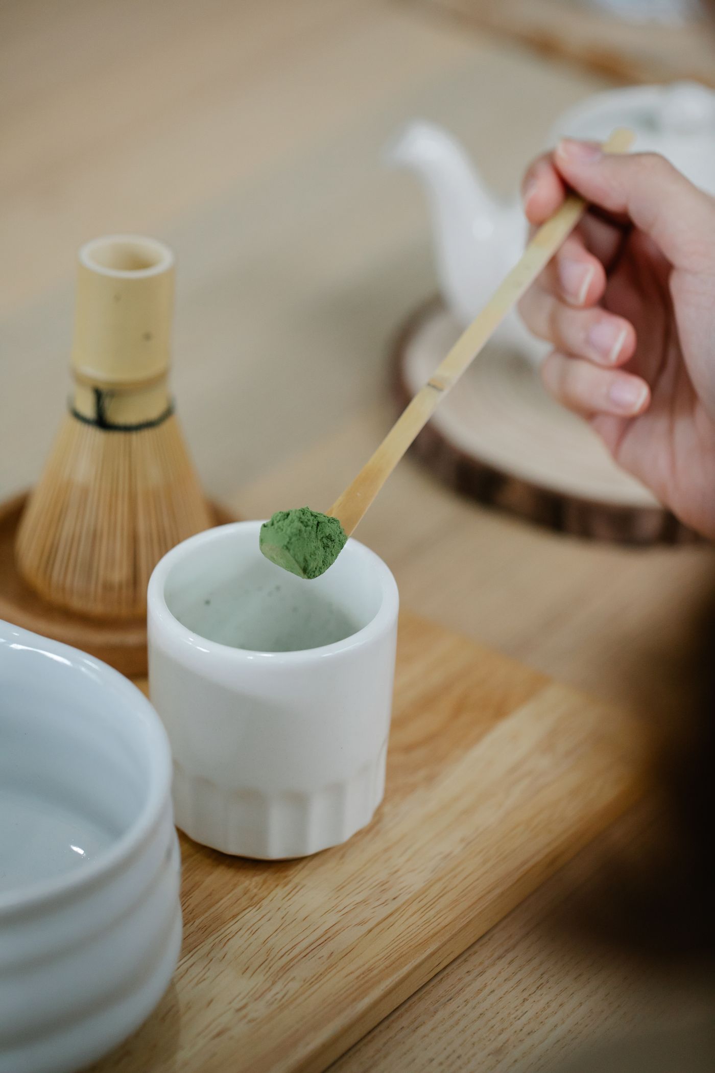 A person scooping matcha powder with a bamboo scoop