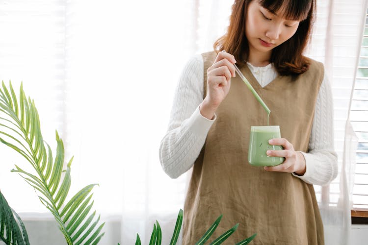 Woman Mixing Green Juice On Clear Glass 