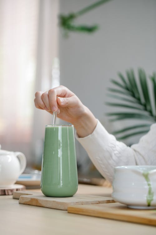 Person Stirring Matcha Drink in Clear Glass 