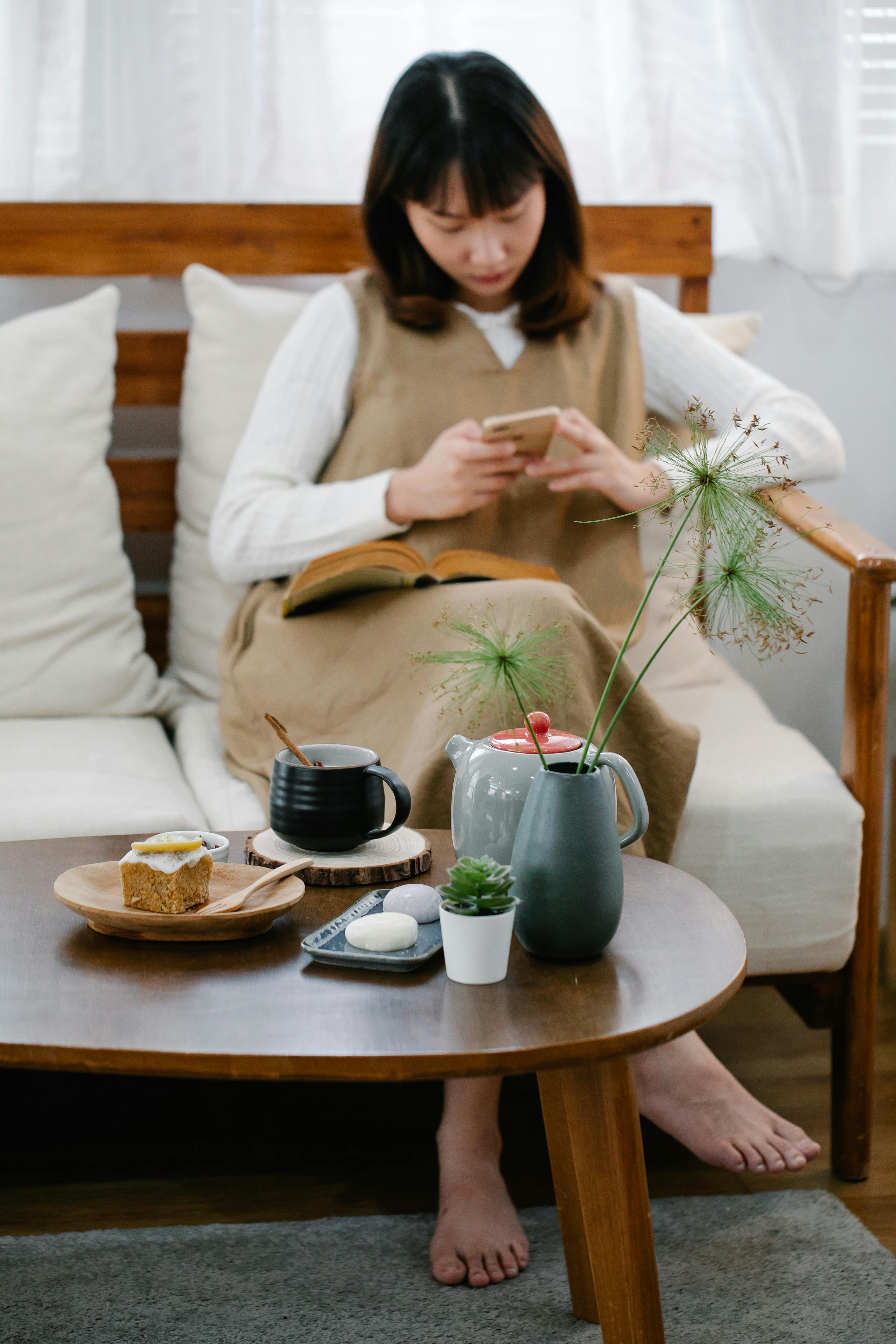 woman sitting on couch texting with breakfast set on coffee table