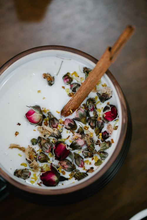 Free A close-up of a creamy herbal tea garnished with rose petals and a cinnamon stick. Stock Photo