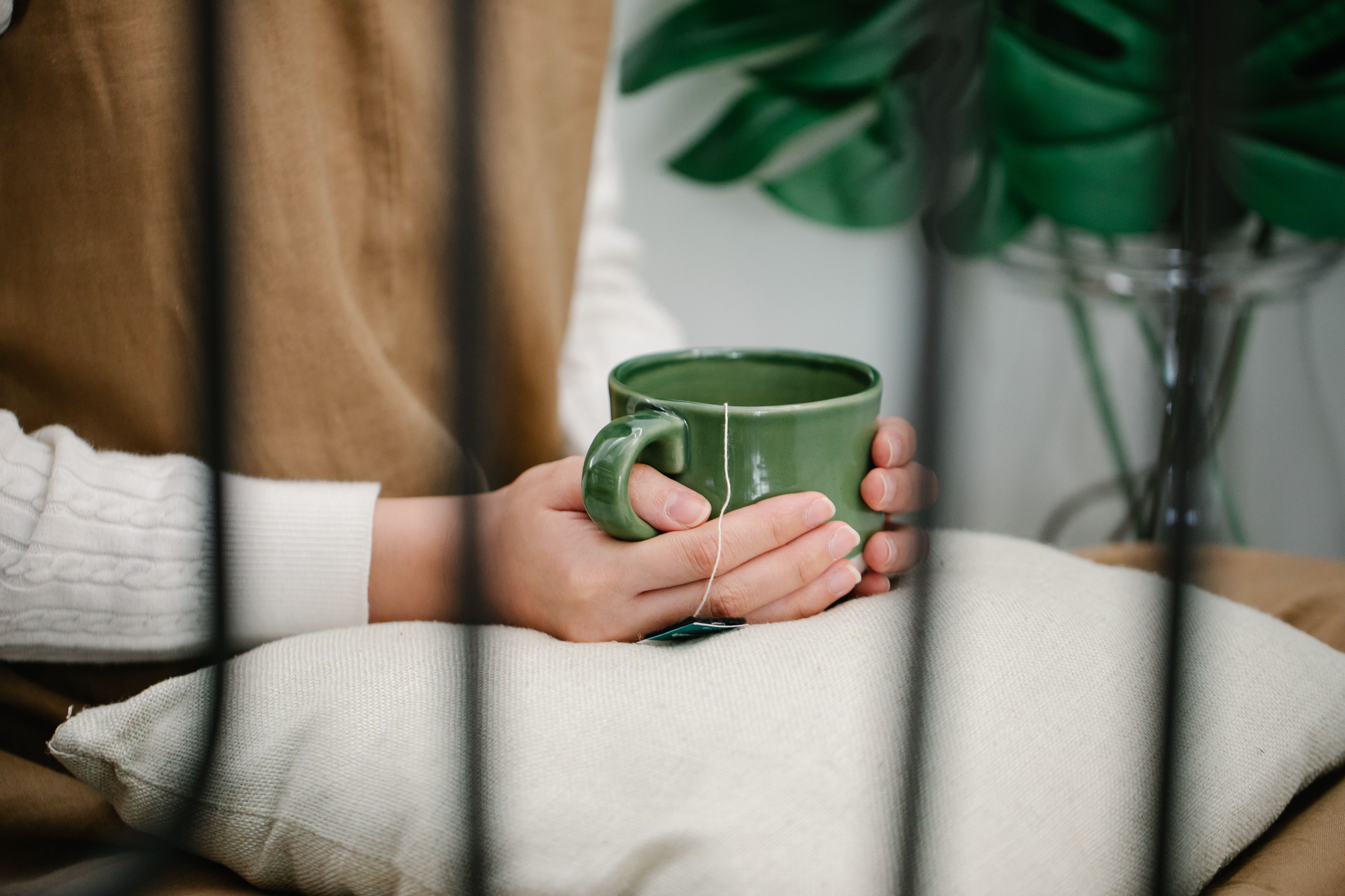 A relaxing indoor moment with hands holding a green mug, resting on a pillow.