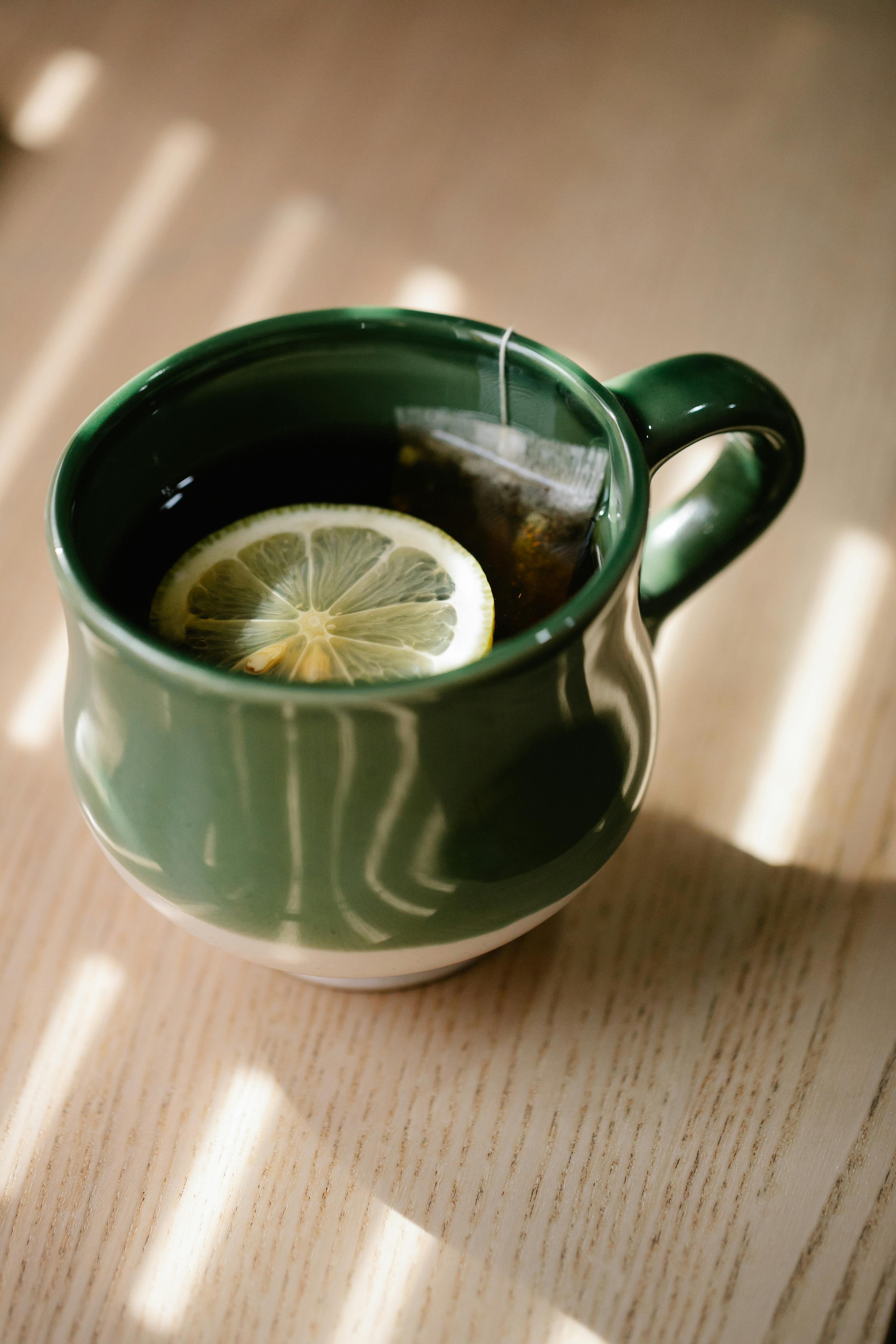 A close-up of lemon tea in a green mug with sunlight streaming through, creating a calming atmosphere.