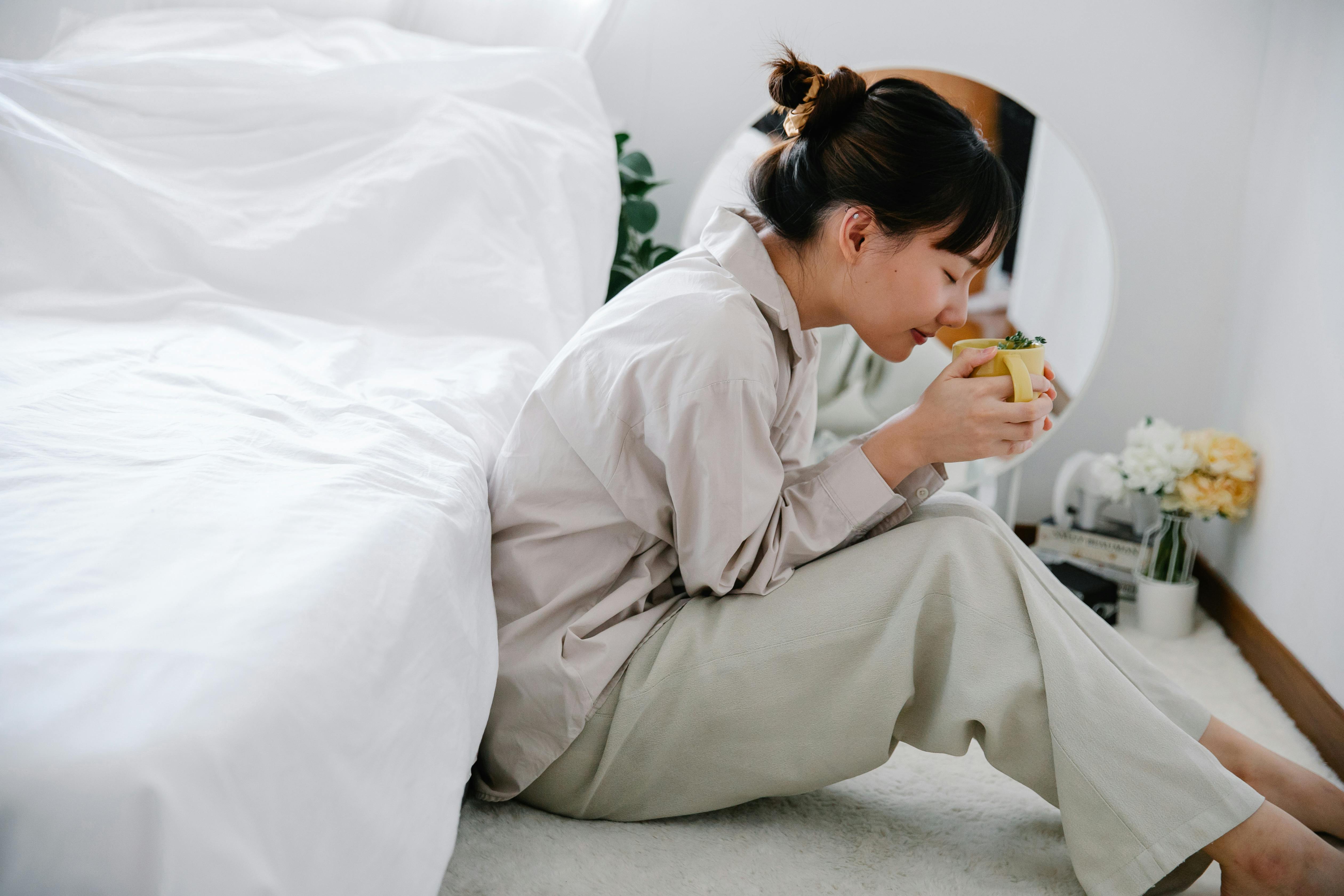 girl sitting by bed and enjoying cup of aromatic tea