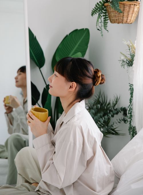 Free Woman enjoying tea indoors surrounded by plants, creating a serene morning ambiance. Stock Photo