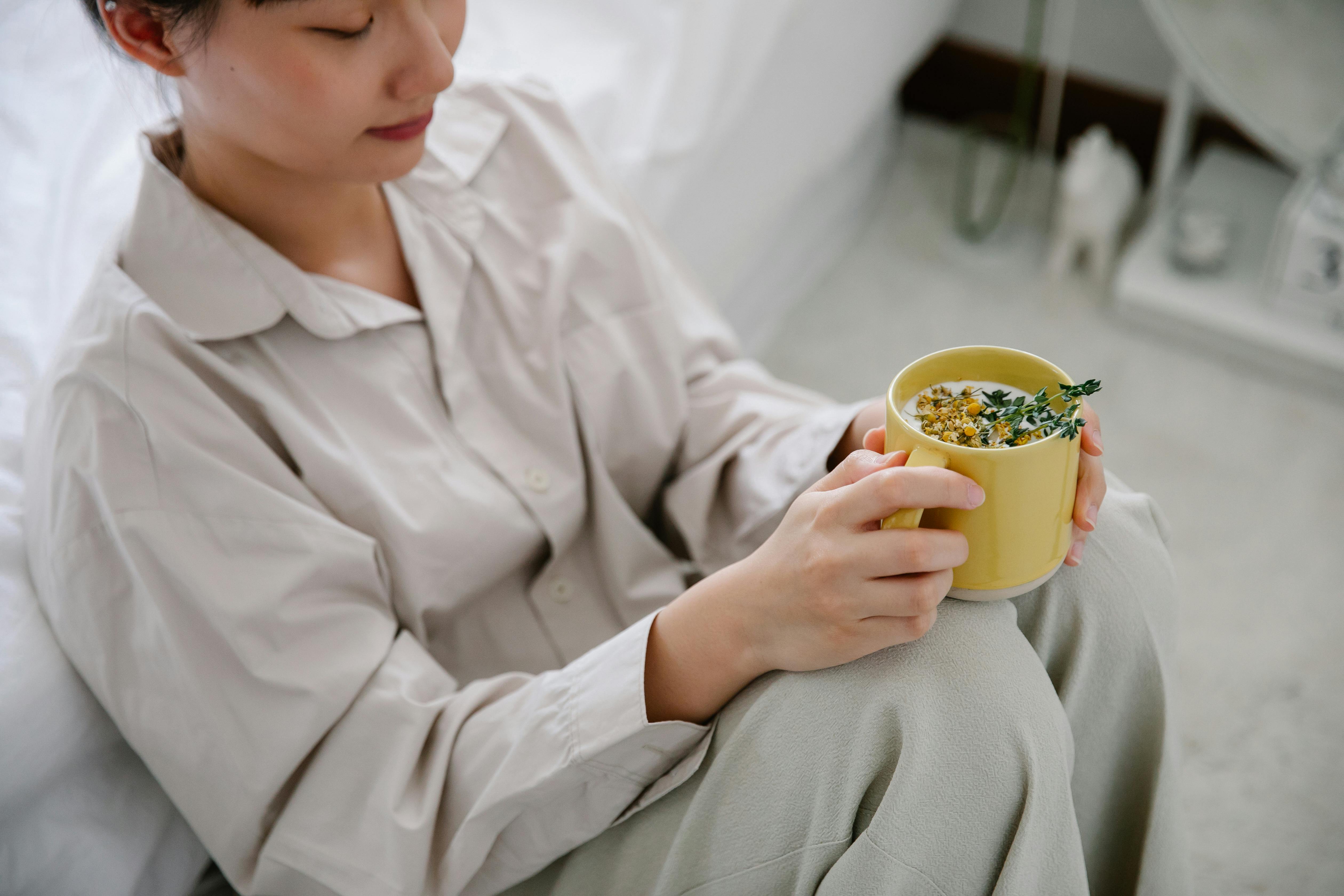 Woman enjoying a hot herbal tea indoors, dressed in cozy sleepwear, promoting relaxation and calm.