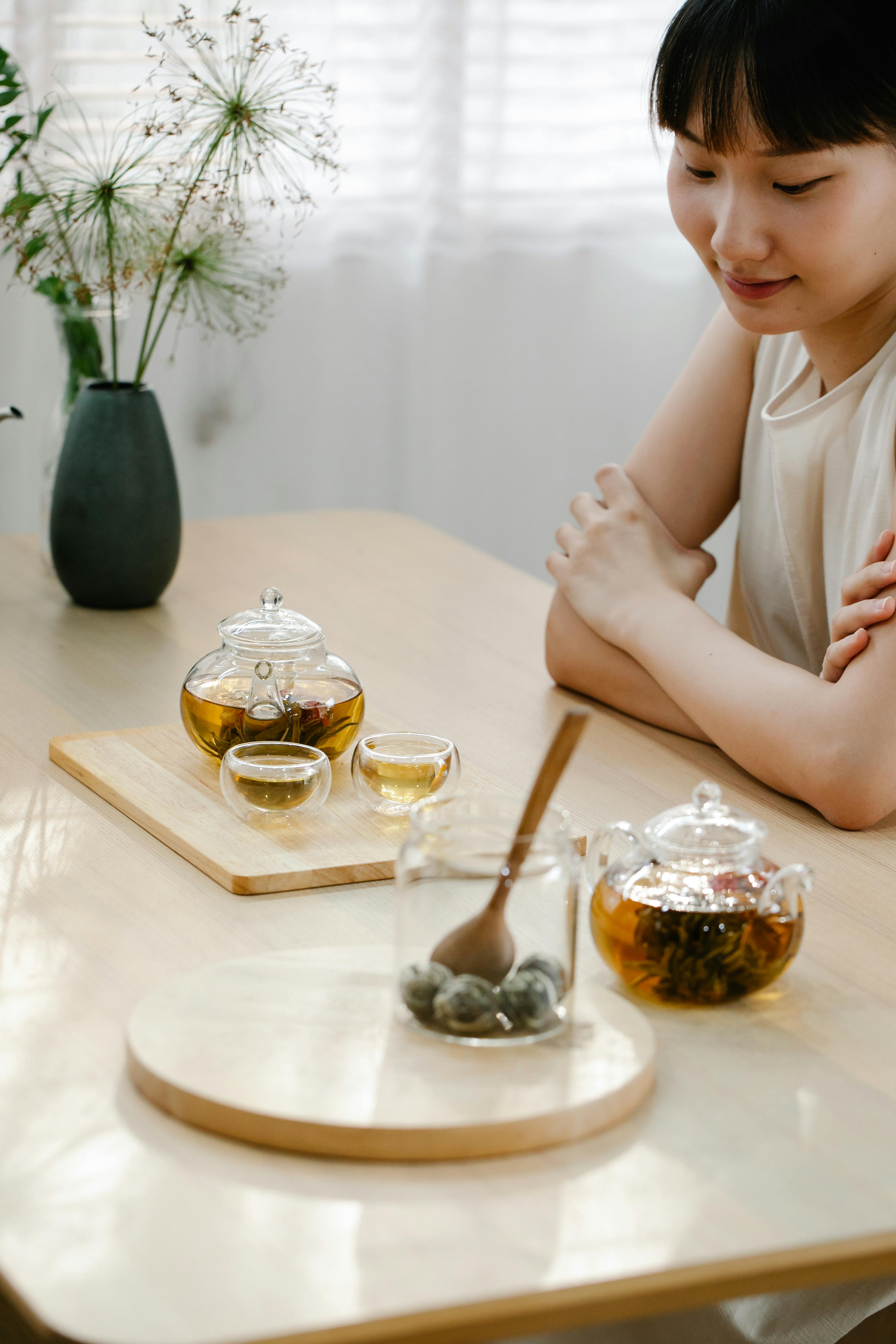 An Asian woman enjoying a serene tea time indoors with elegant teapots and plants.
