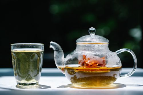 Free A glass teapot filled with herbal tea next to a transparent glass under sunlight. Refreshing and aromatic. Stock Photo