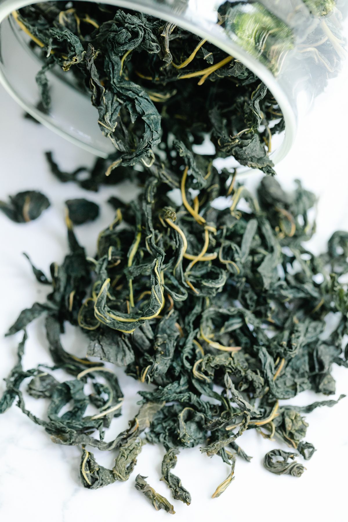 Loose green tea leaves from a glass jar on white