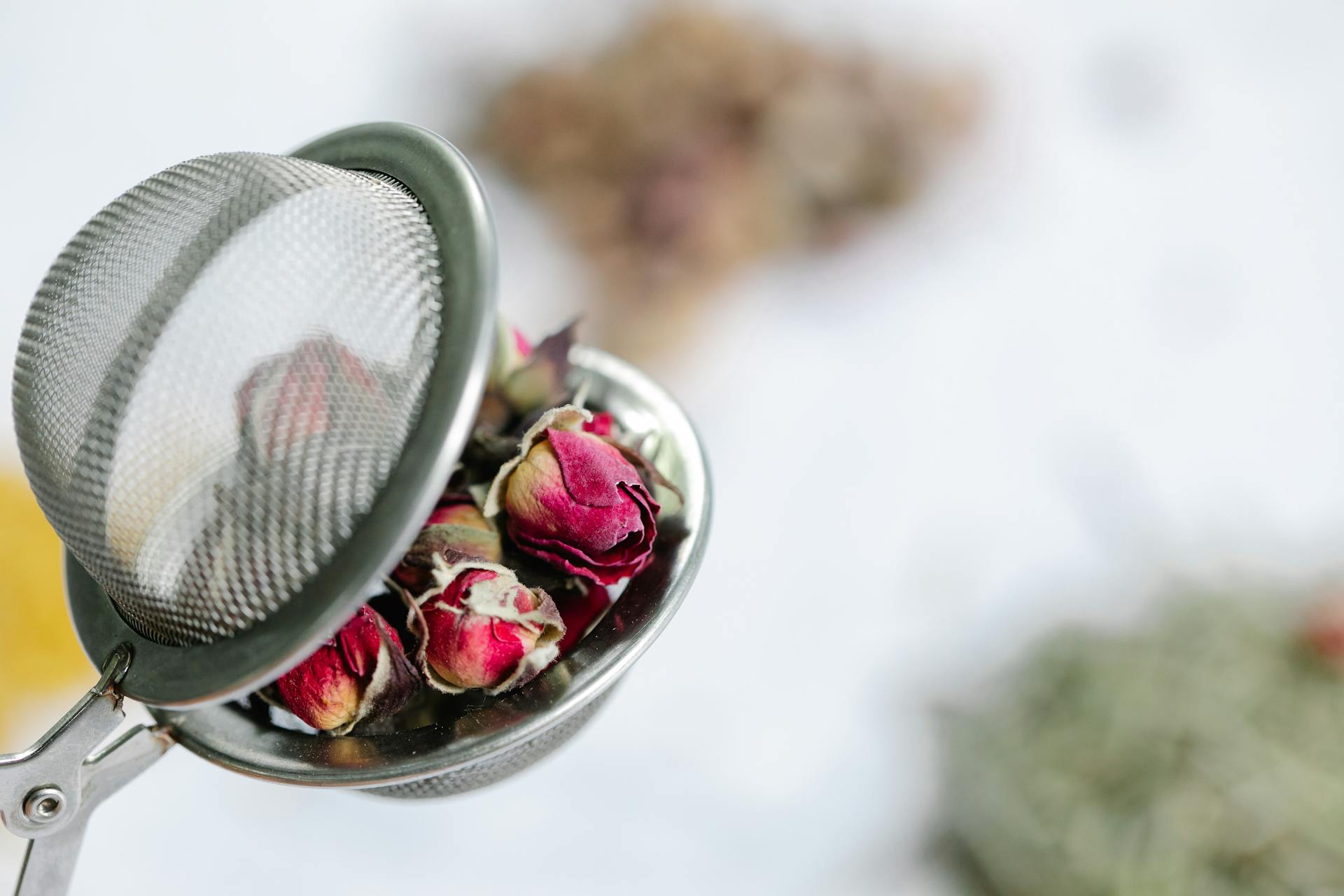 Delicate dried rosebuds in a mesh tea infuser, perfect for herbal teas.